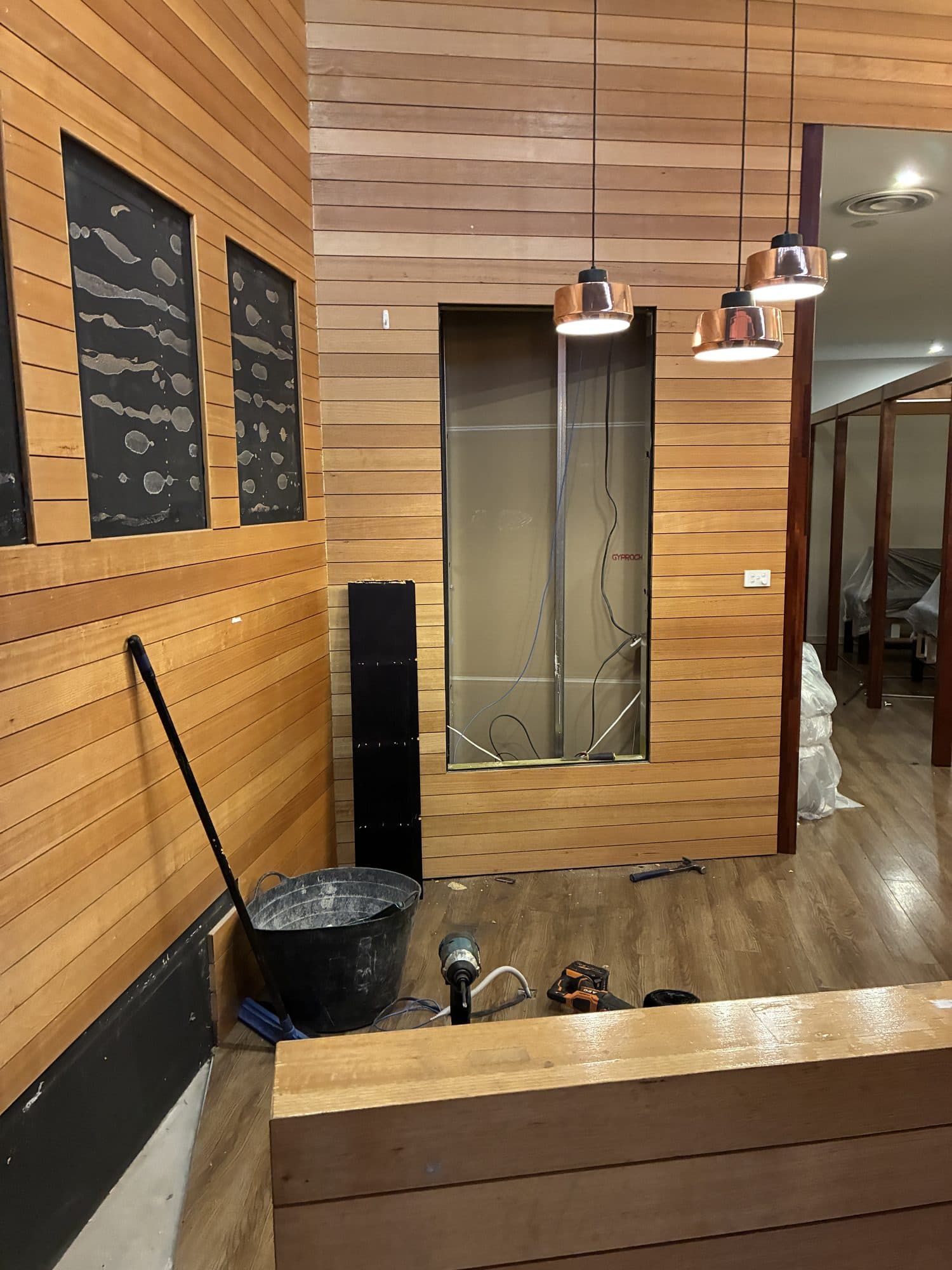 A timber-lined wall with copper pendant lights and a timber counter