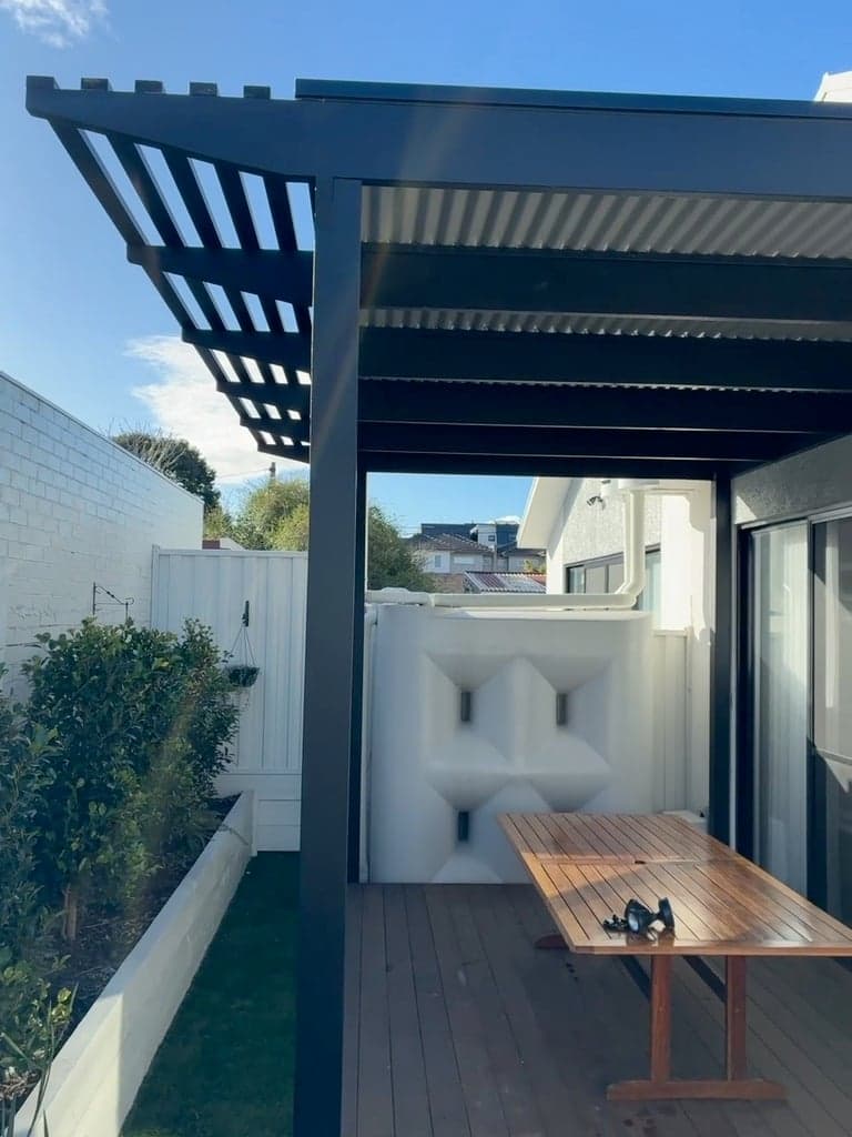 A timber pergola over a deck, with an open slatted end section and a planter bed