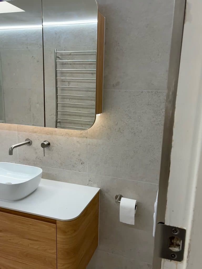 A timber vanity with a white top, vessel basin and backlit mirror cabinet