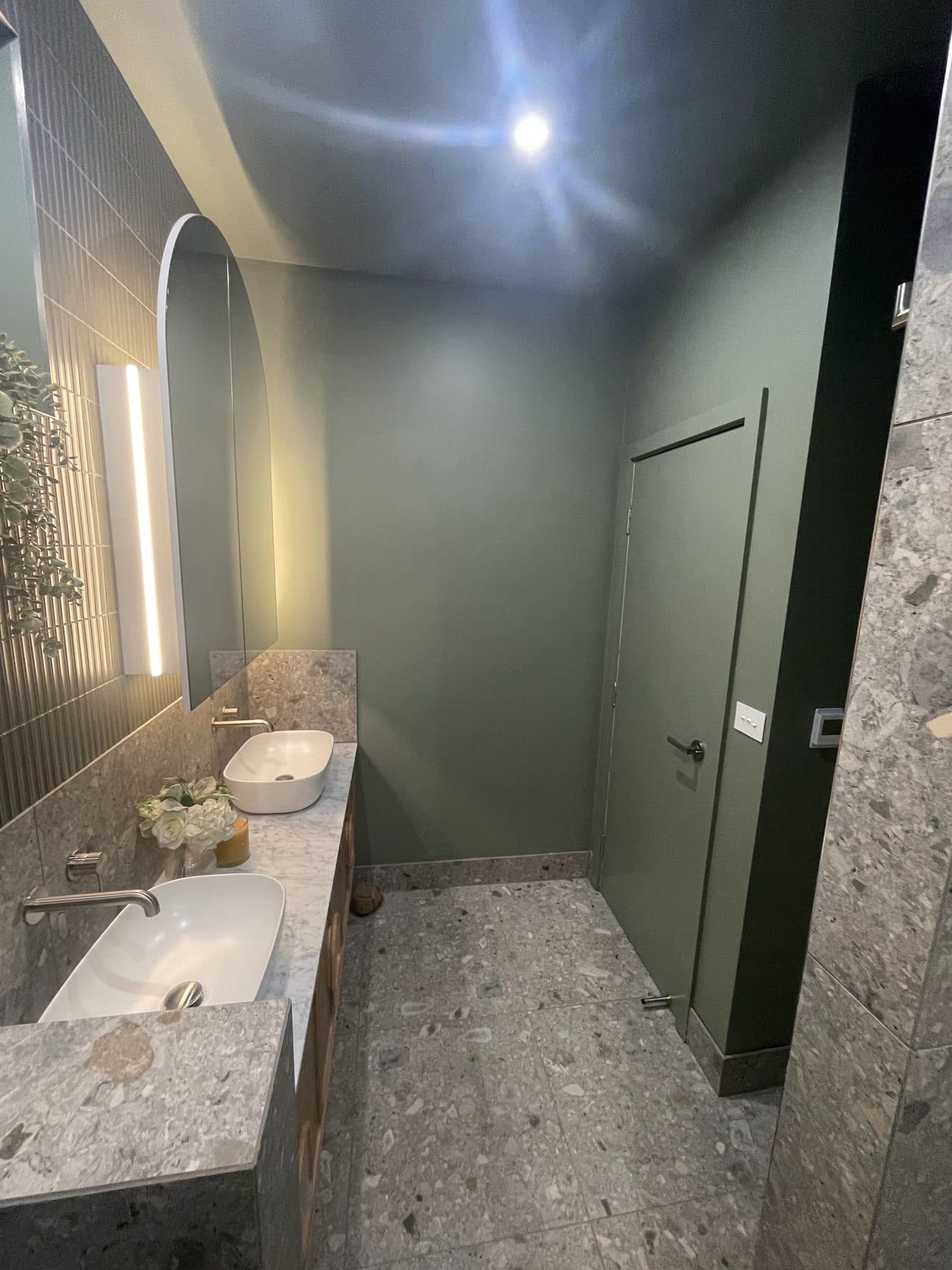 A green-walled bathroom with a terrazzo floor and an arched mirror