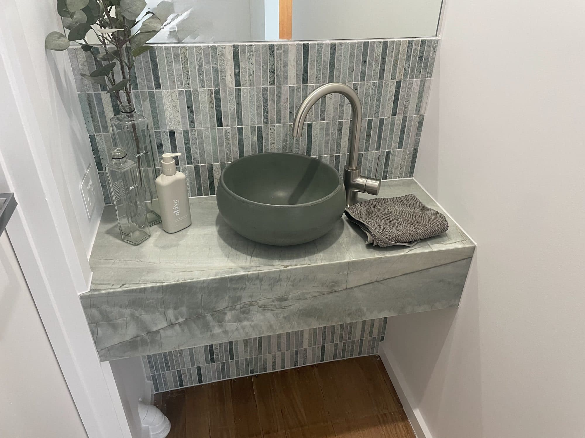 A powder room with a green bowl basin on a stone bench against mosaic tile
