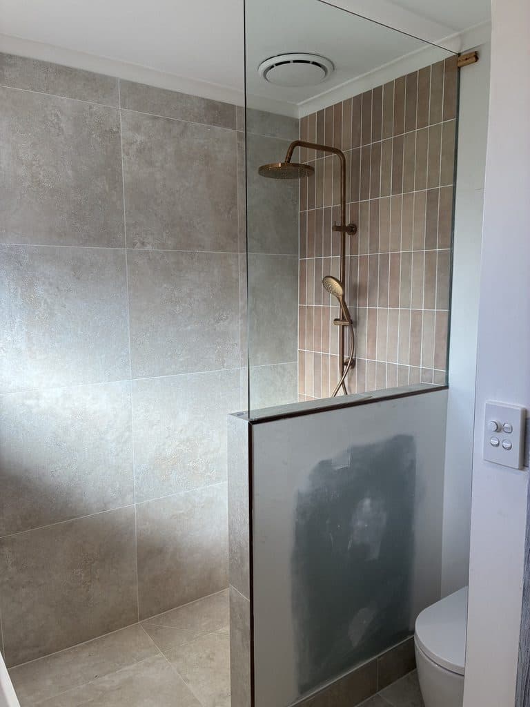 A walk-in shower with a rail shower, terracotta feature tiles and a glass panel