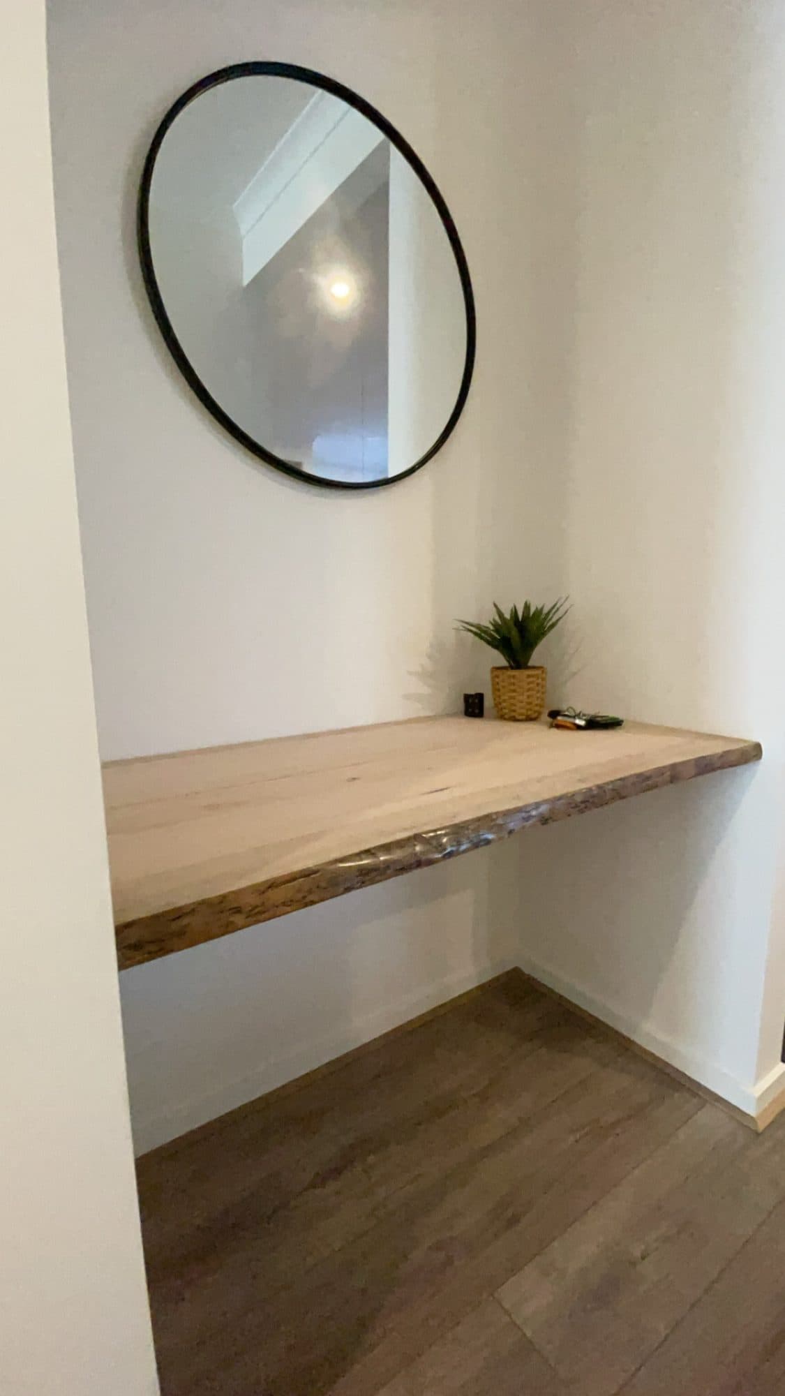 A live-edge timber desk set into a wall, with a round mirror above