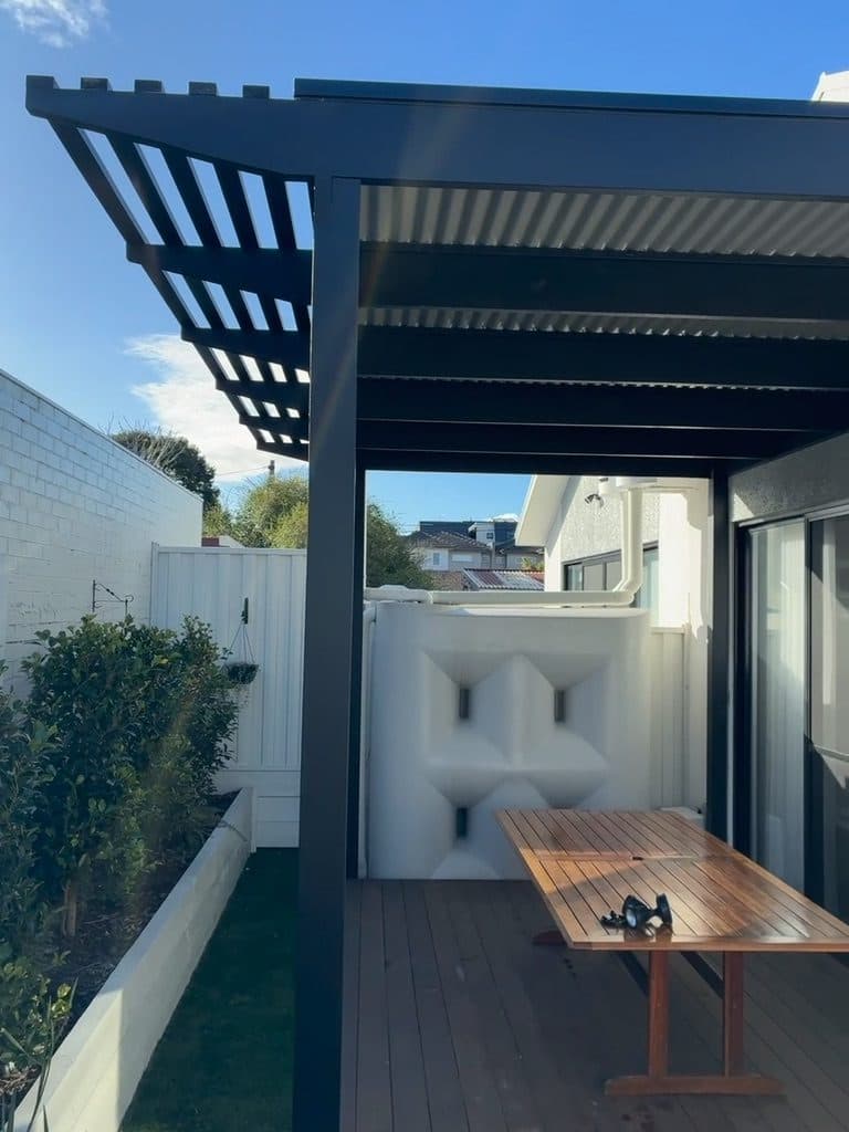 A deck under a timber pergola beside a planter bed