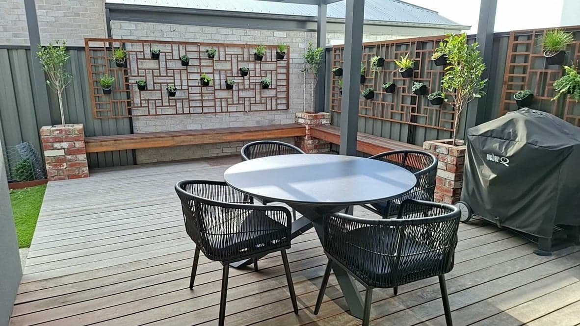 A timber deck with an outdoor table in front of a decorative planter wall