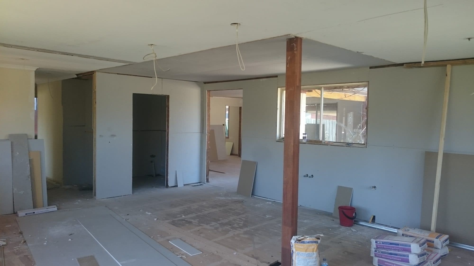 An open-plan room lined with new plasterboard, with a timber post and door openings