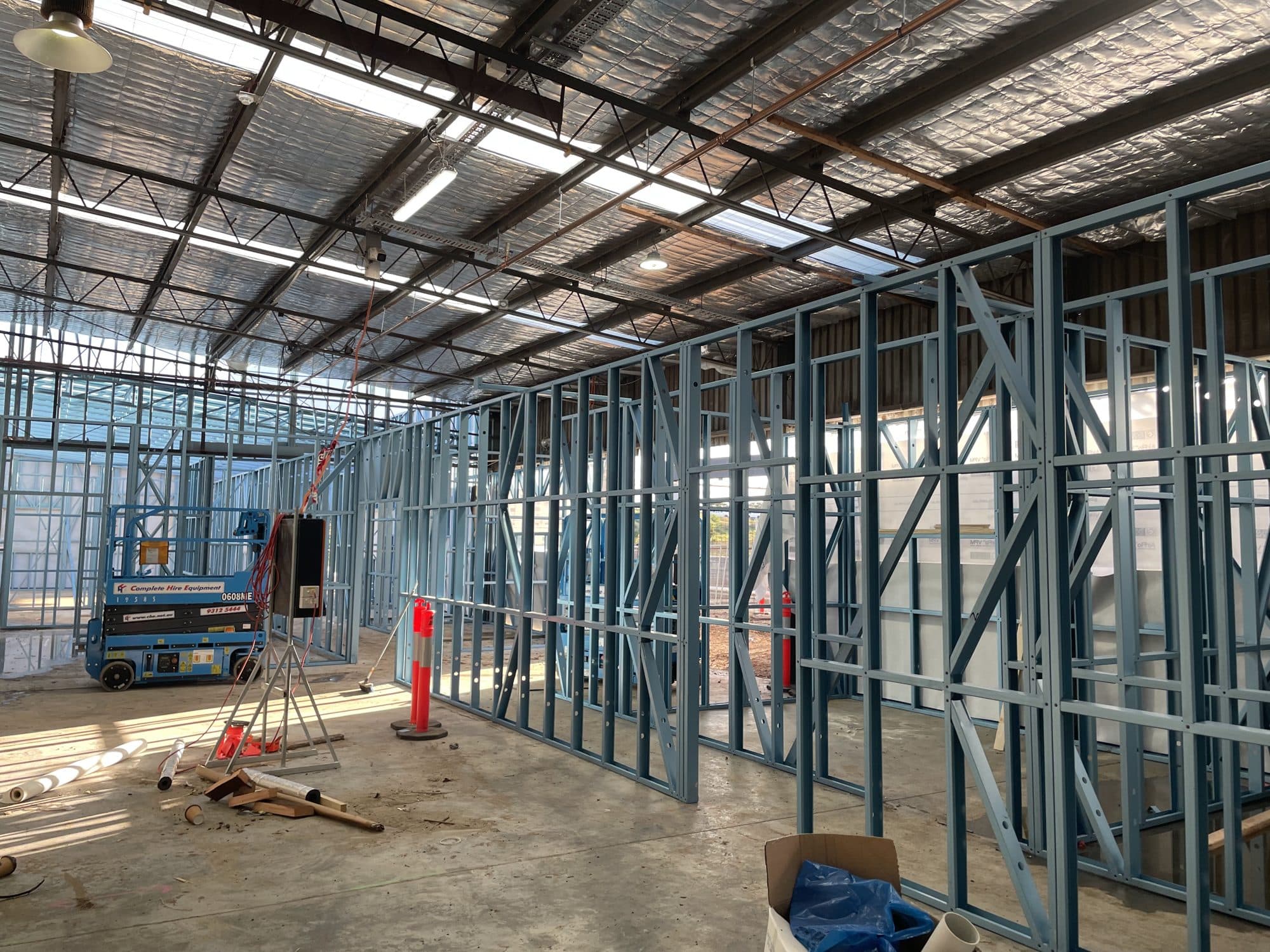 Rows of steel stud walls inside a warehouse, with a scissor lift