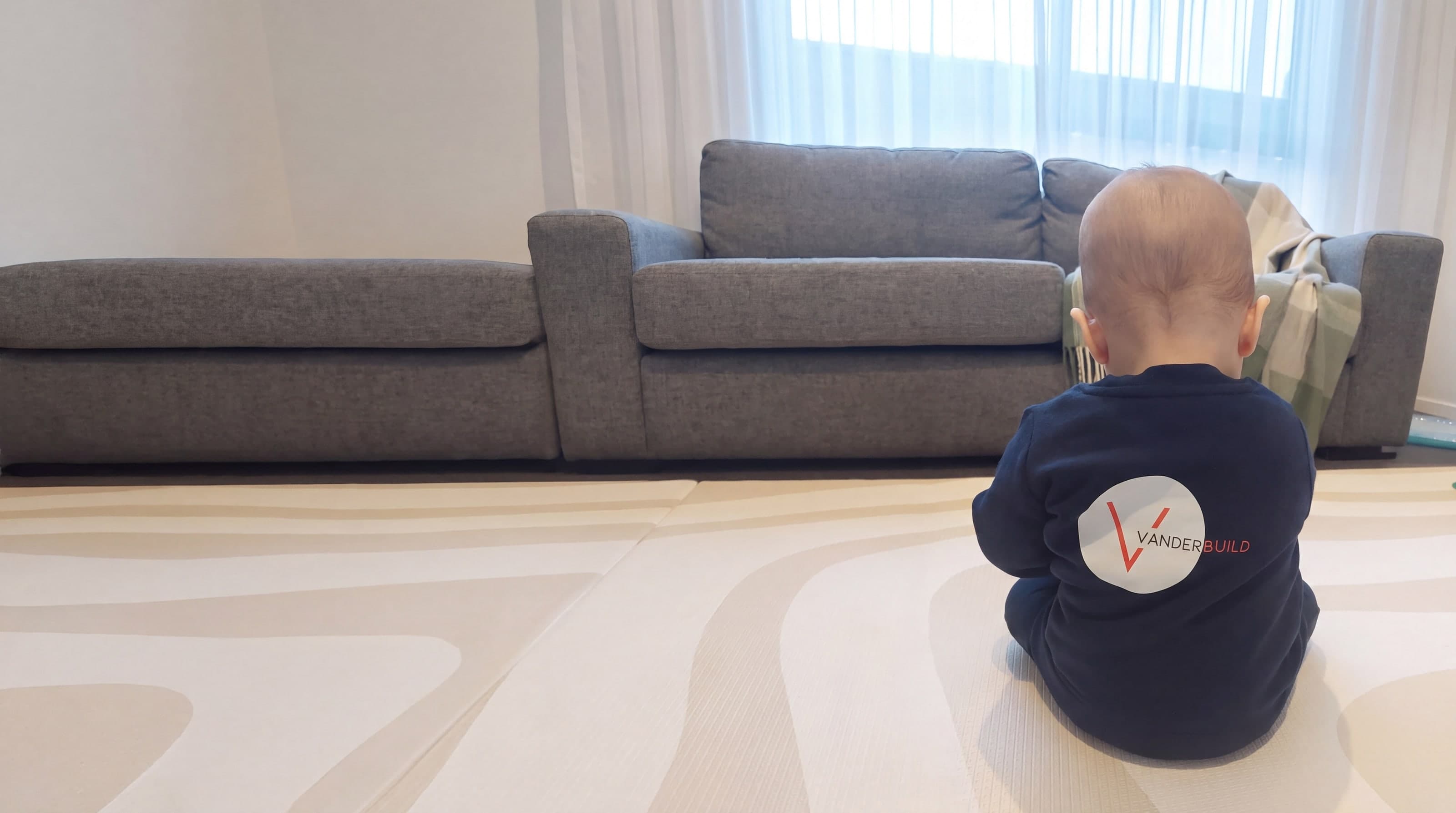 Ryan's child sitting on a rug, seen from behind, wearing a navy jumper with the VANDERBUILD logo