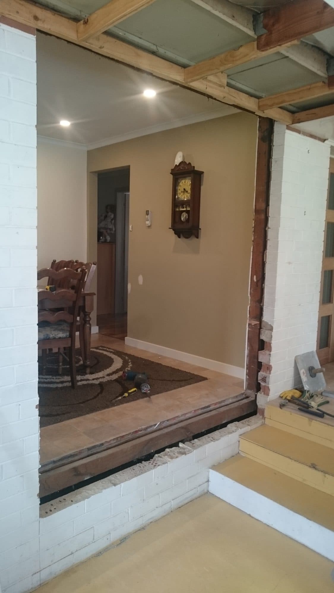 A wide opening cut through a painted brick wall into the dining room on the higher level