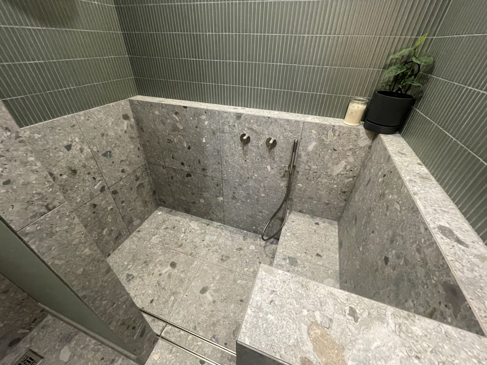 A finished shower with terrazzo tiles, a tiled bench and green wall tiles