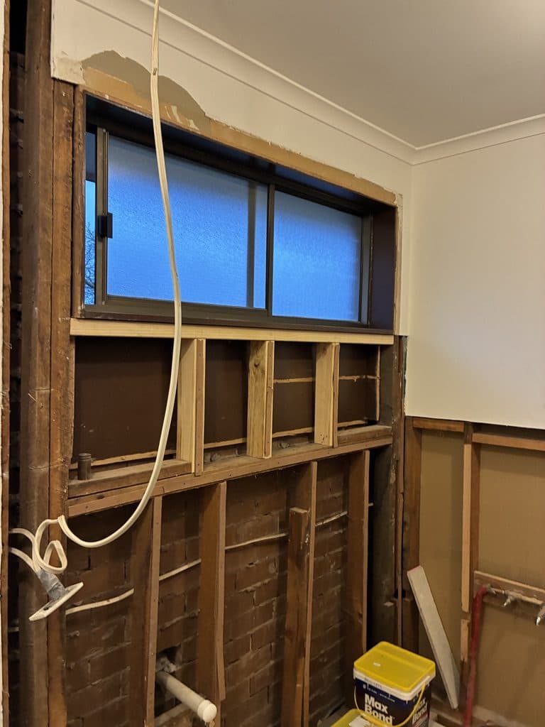 The window wall with old linings removed and pipes exposed