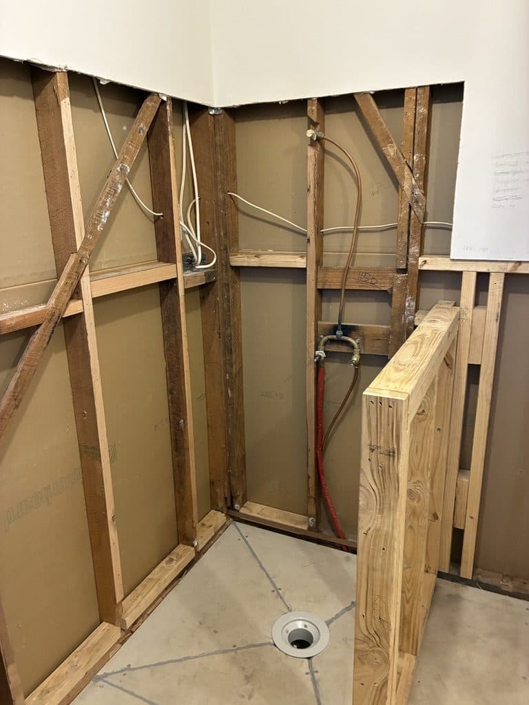Plumbing roughed in behind new framing, with a floor waste in place