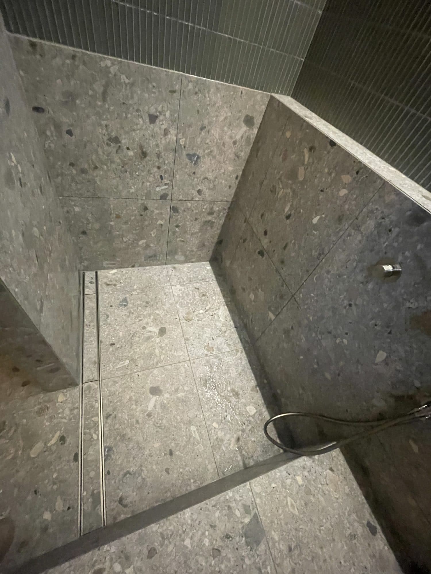 The shower floor in terrazzo-look tile, falling to a linear drain beside the tiled step