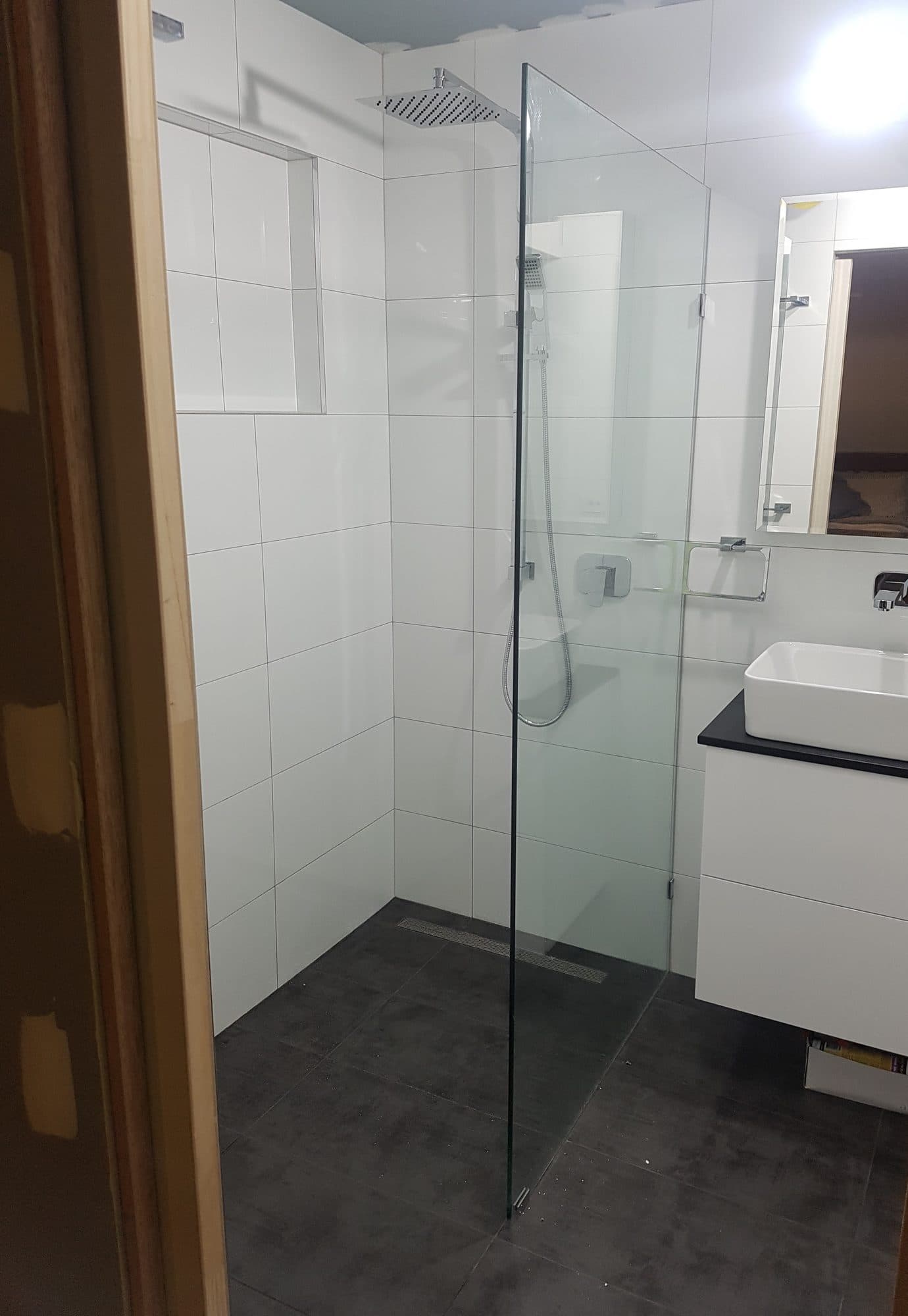 A walk-in shower with a fixed glass panel beside a white vanity