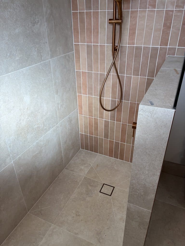 A walk-in shower with pink vertical tile and a rail shower