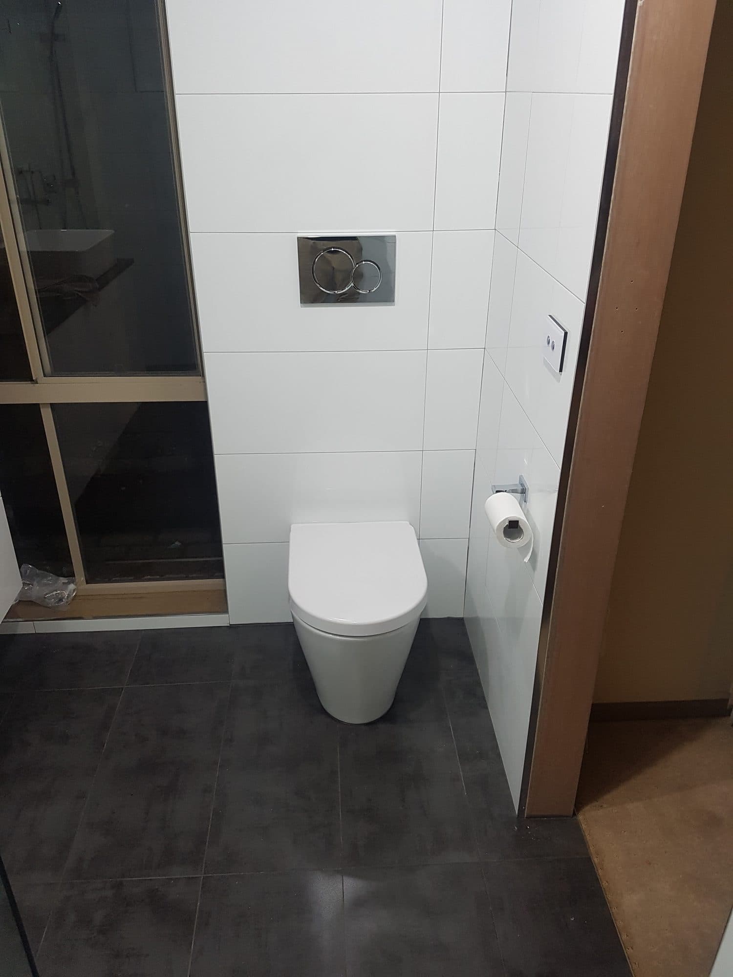 A wall-hung toilet against white tile, with a dark tiled floor