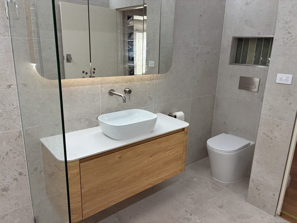 A floating timber vanity beside a toilet and a green-tiled niche