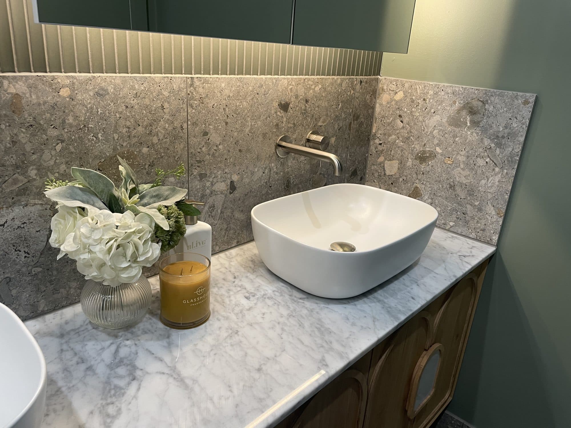 A finished vanity with a white basin on a marble top, against terrazzo tile