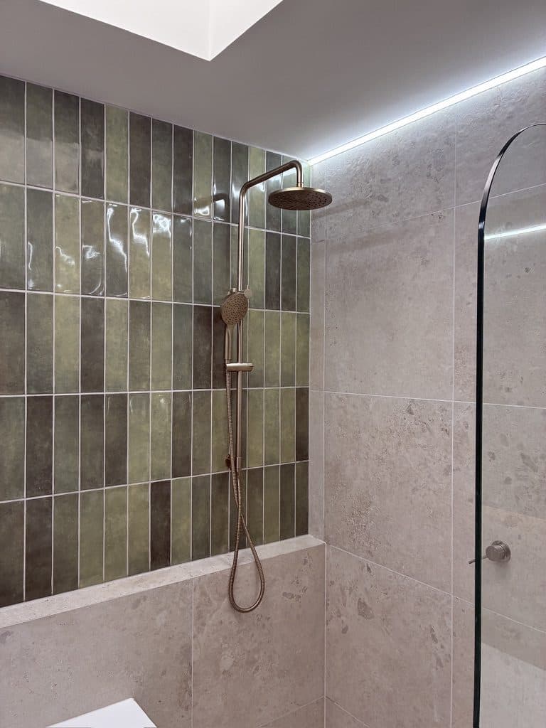 A shower wall in green vertical tile with a rail shower