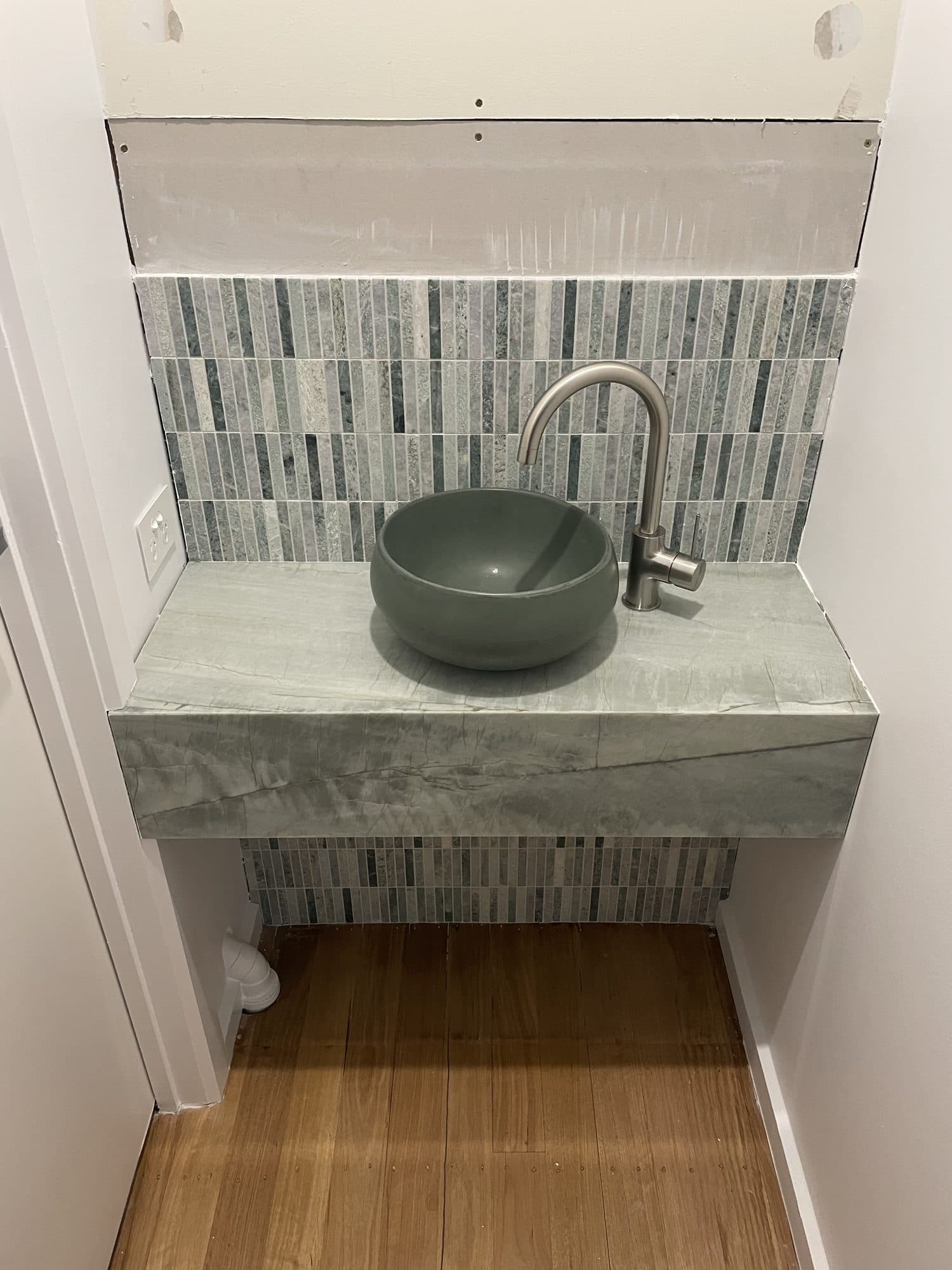 A stone-clad floating bench with a green bowl basin and mosaic splashback