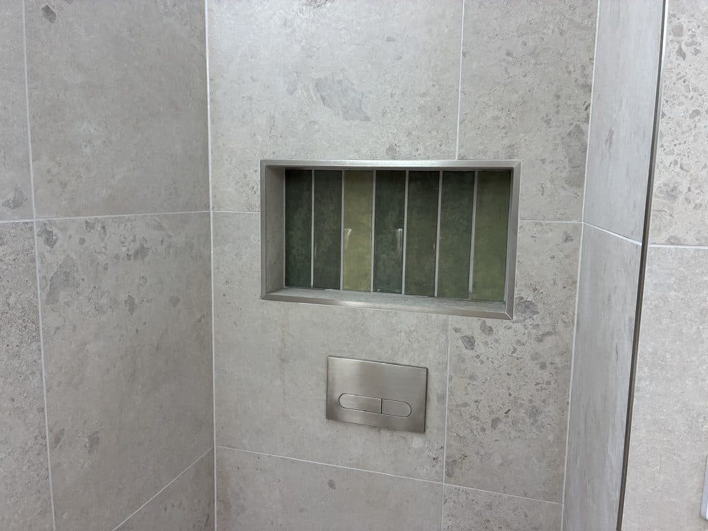 A tiled niche lined in green tile above the toilet flush plate