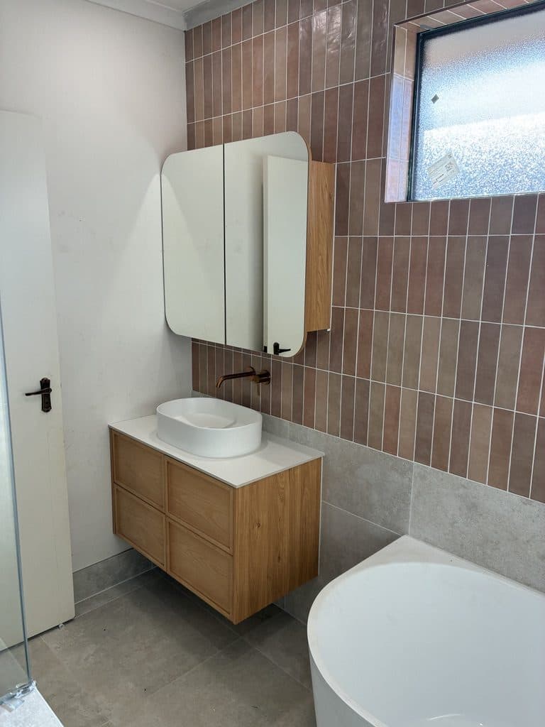 A timber vanity with a basin and a mirror cabinet beside the bath