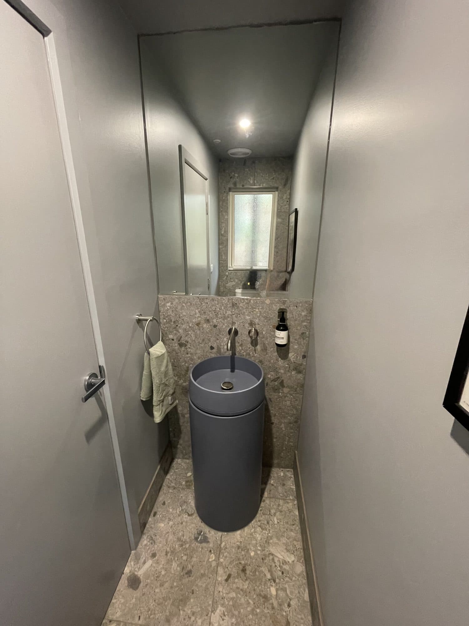 A narrow toilet room with a round pedestal basin