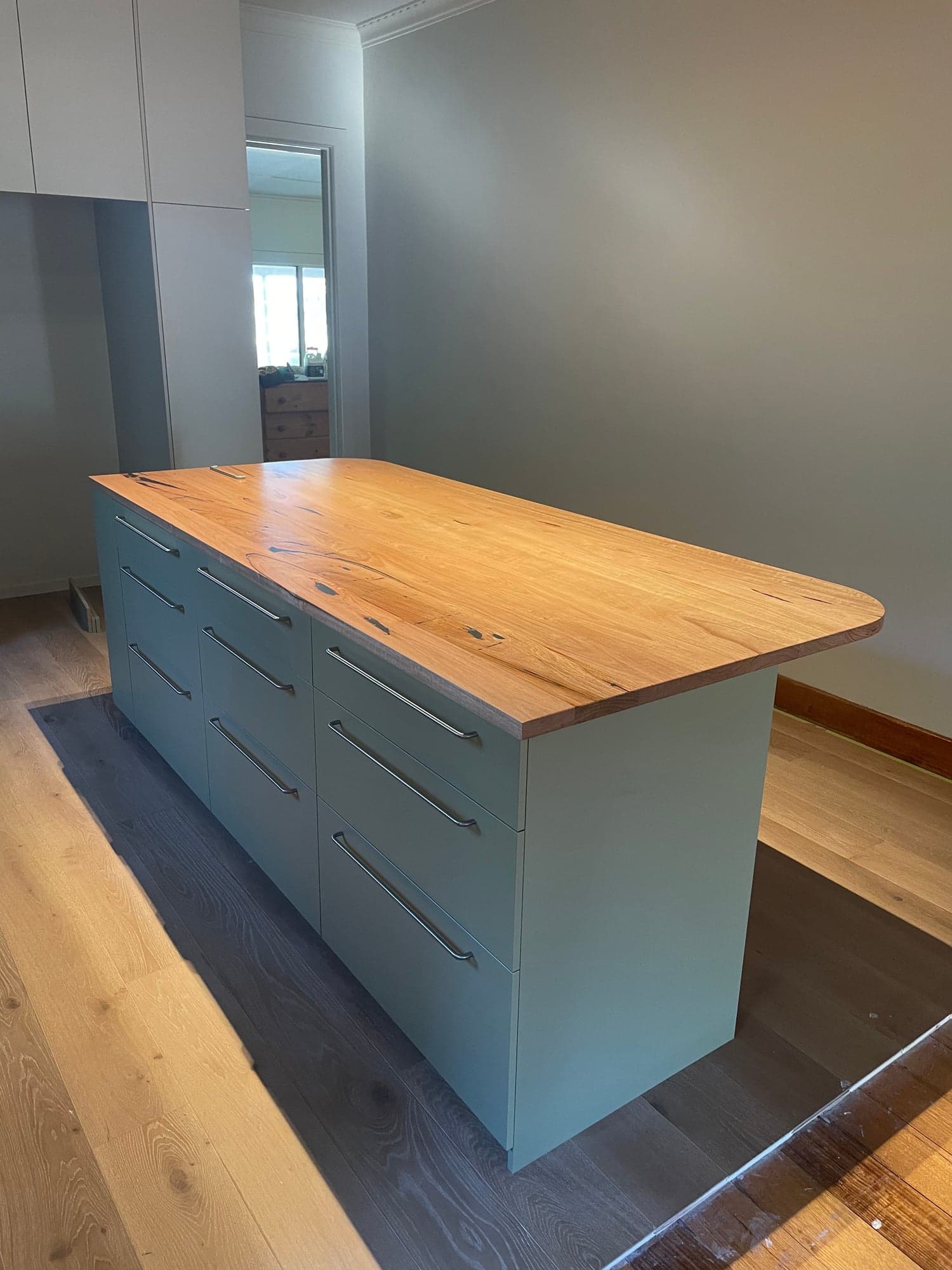 The kitchen island with a timber top on a sage-green cabinet