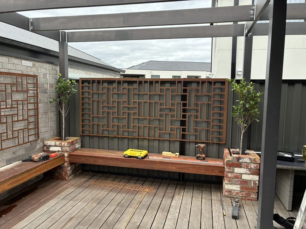 A back yard with a timber deck, planter wall and synthetic lawn