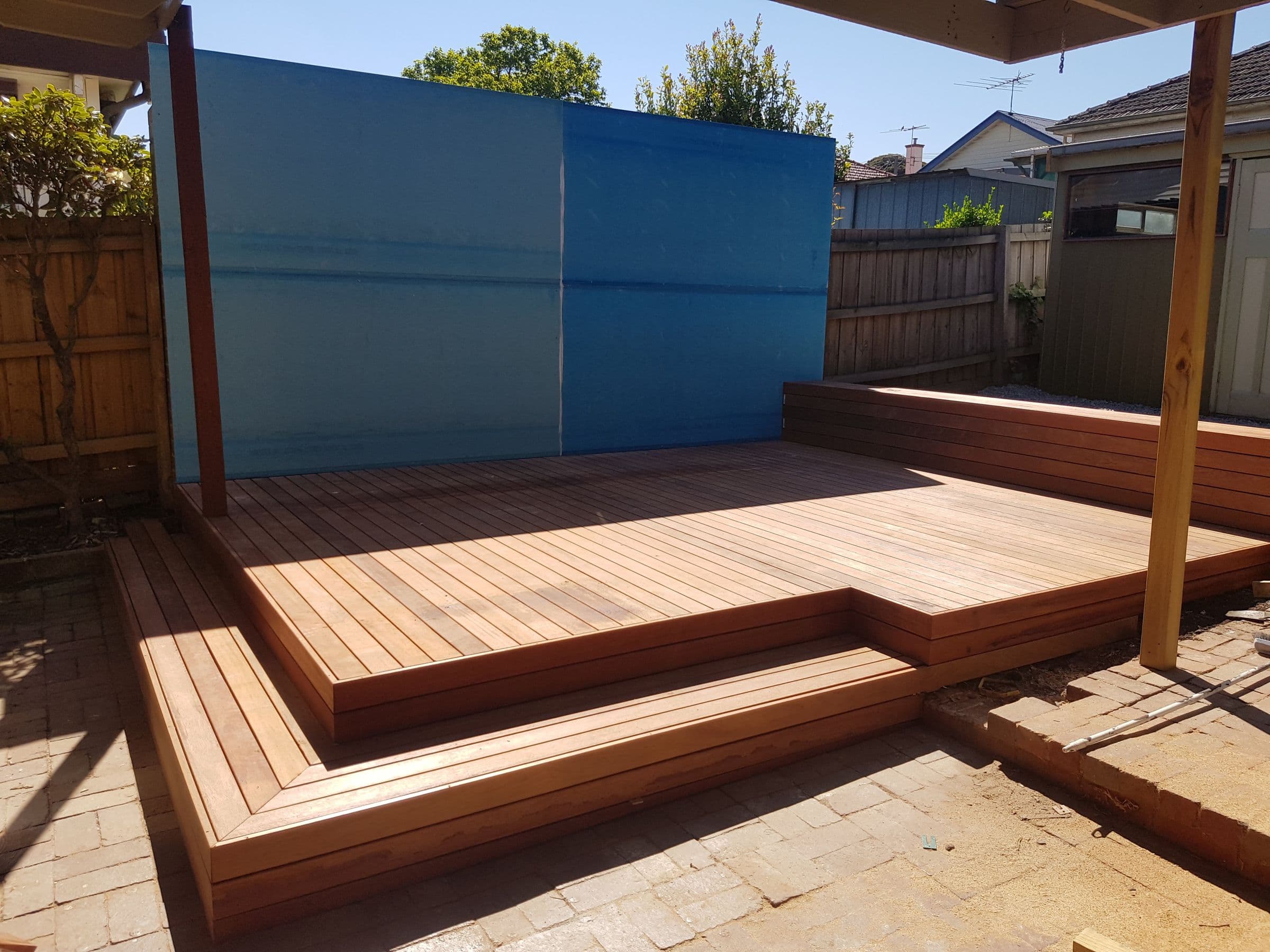 A new hardwood deck built in two steps down to the paving, under a timber pergola